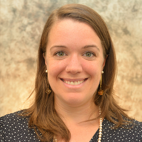 Woman wearing a navy and white polka dot top in front of a tan background