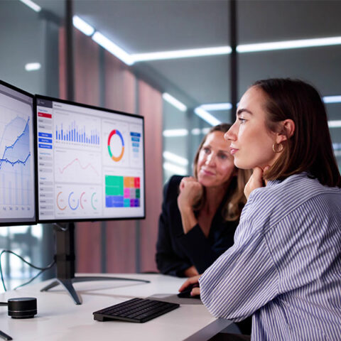 Two women in front of computer with data driven visuals