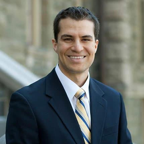 Gustavo Flores-Macias wearing a navy suit standing in front of a stone stairwell