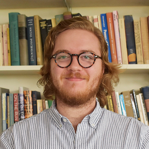 Man wearing a collard shirt and glasses in front of bookshelf