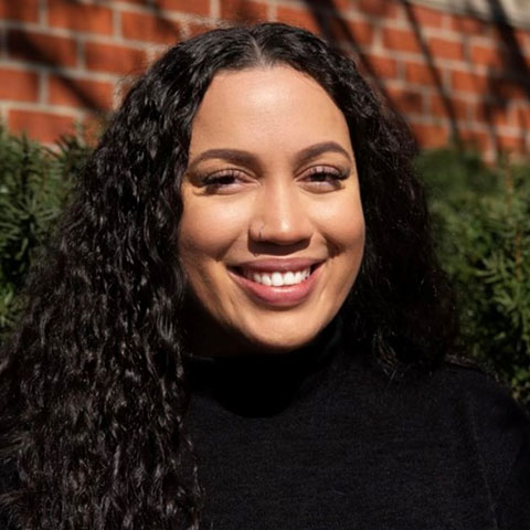 Woman wearing a black turtleneck standing in front of a brick wall