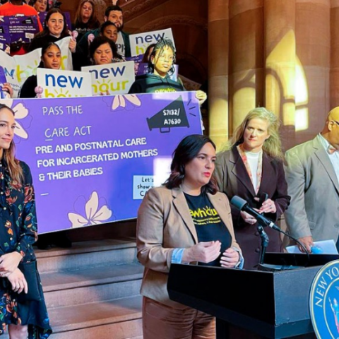 Woman standing at podium with group of supporters behind her