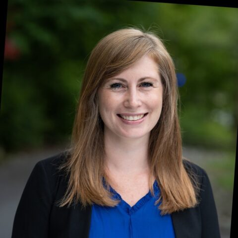 Woman smiling at camera wearing a black blazer and blue shirt