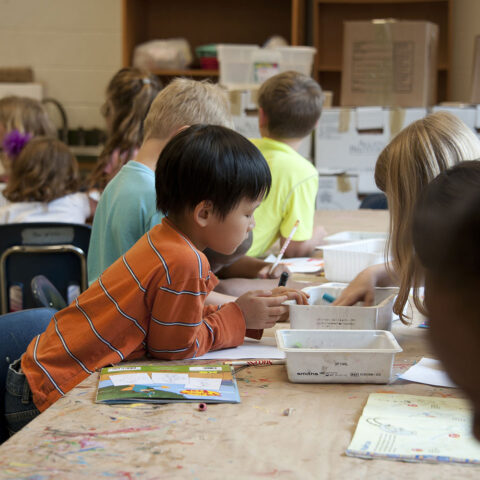 A group of children sitting a tables, drawing with pencils and markers