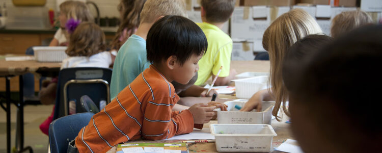 A group of children sitting a tables, drawing with pencils and markers