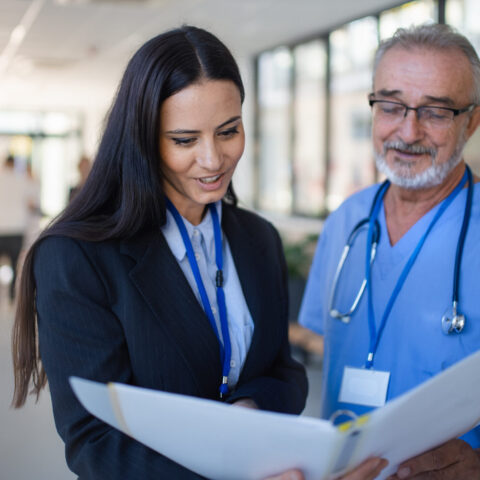 Two healthcare professionals reviewing a document in a hospital corridor.